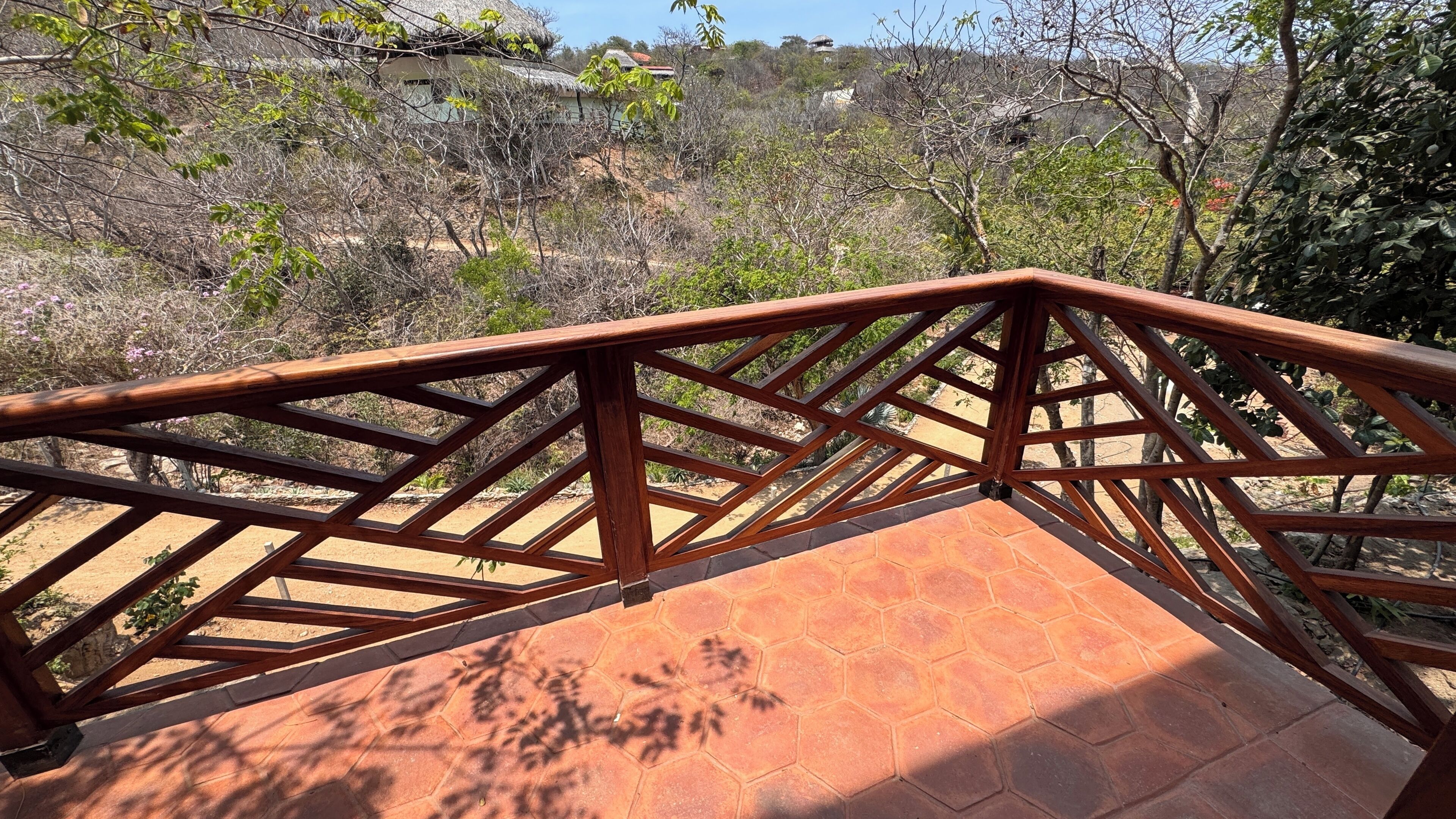 A wooden balcony with a geometric railing overlooking a dry, hilly landscape with sparse vegetation.