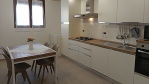 A modern kitchen with white cabinets, a gas stove, and a microwave. There is a dining table with chairs and a vase of flowers. - A&F House - Ale (Torricella)