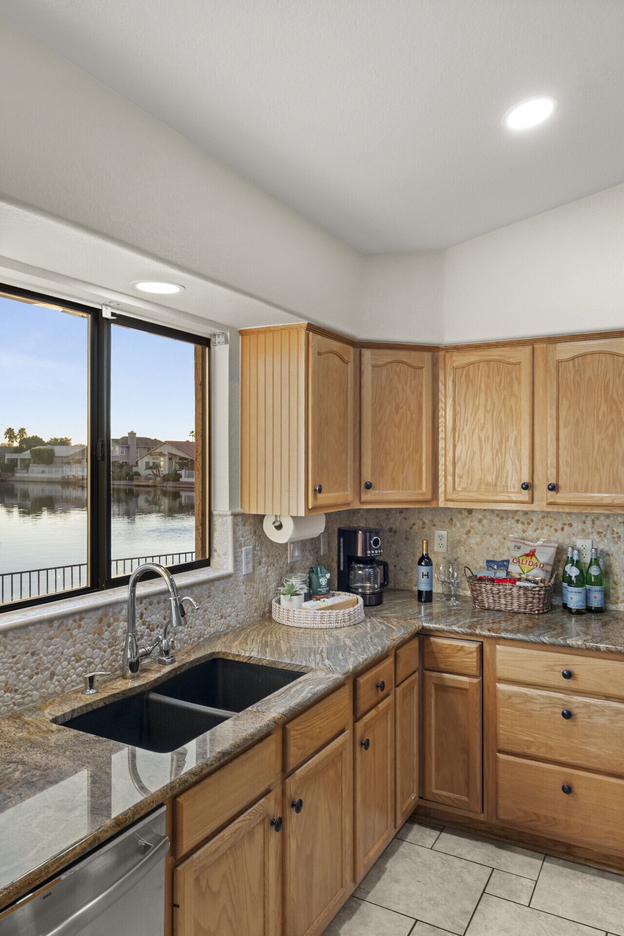 A kitchen with wooden cabinets, a granite countertop, a built-in sink, and a window overlooking a body of water.
