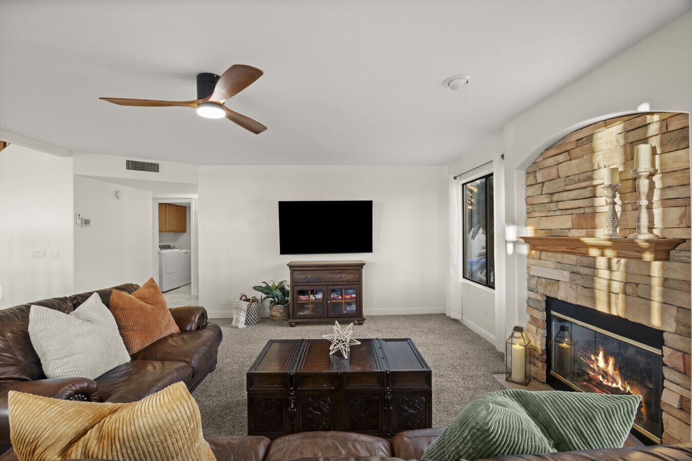 A living room with a fireplace, a flat-screen TV mounted on the wall, a leather sofa, and a ceiling fan.