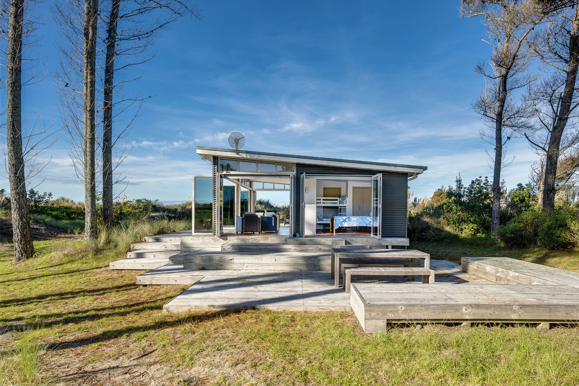 Une cabane moderne à plan ouvert, dotée d’une entrée avec porte vitrée, d’une petite terrasse et offrant une vue sur le paysage environnant.