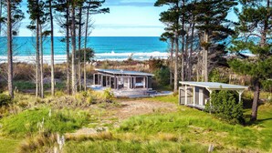 A coastal property with two cabins, one with a glass facade and the other with a wooden exterior, surrounded by pine trees and overlooking the ocean.