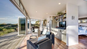 A modern open-plan living area with a kitchen, dining space, and a large glass door leading to a deck.