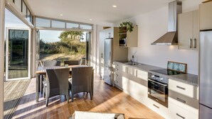 A modern kitchen with a large window, a dining area with wicker chairs, and a view of the outdoors.