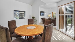 A dining area with a round wooden table and six chairs, a small side table with a plant, and a view through a sliding glass door to a balcony.