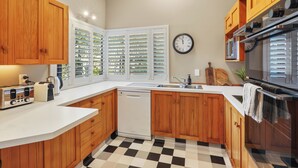 A kitchen with wooden cabinets, a white countertop, a black and white checkered floor, a clock, and a stove.