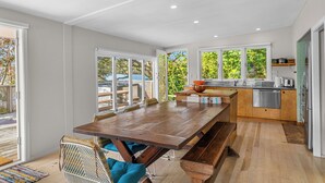 A modern kitchen with a wooden table and bench, large windows, and a view of the outdoors. - Herons Hideaway - Snells Beach Holiday Home (Snells Beach)