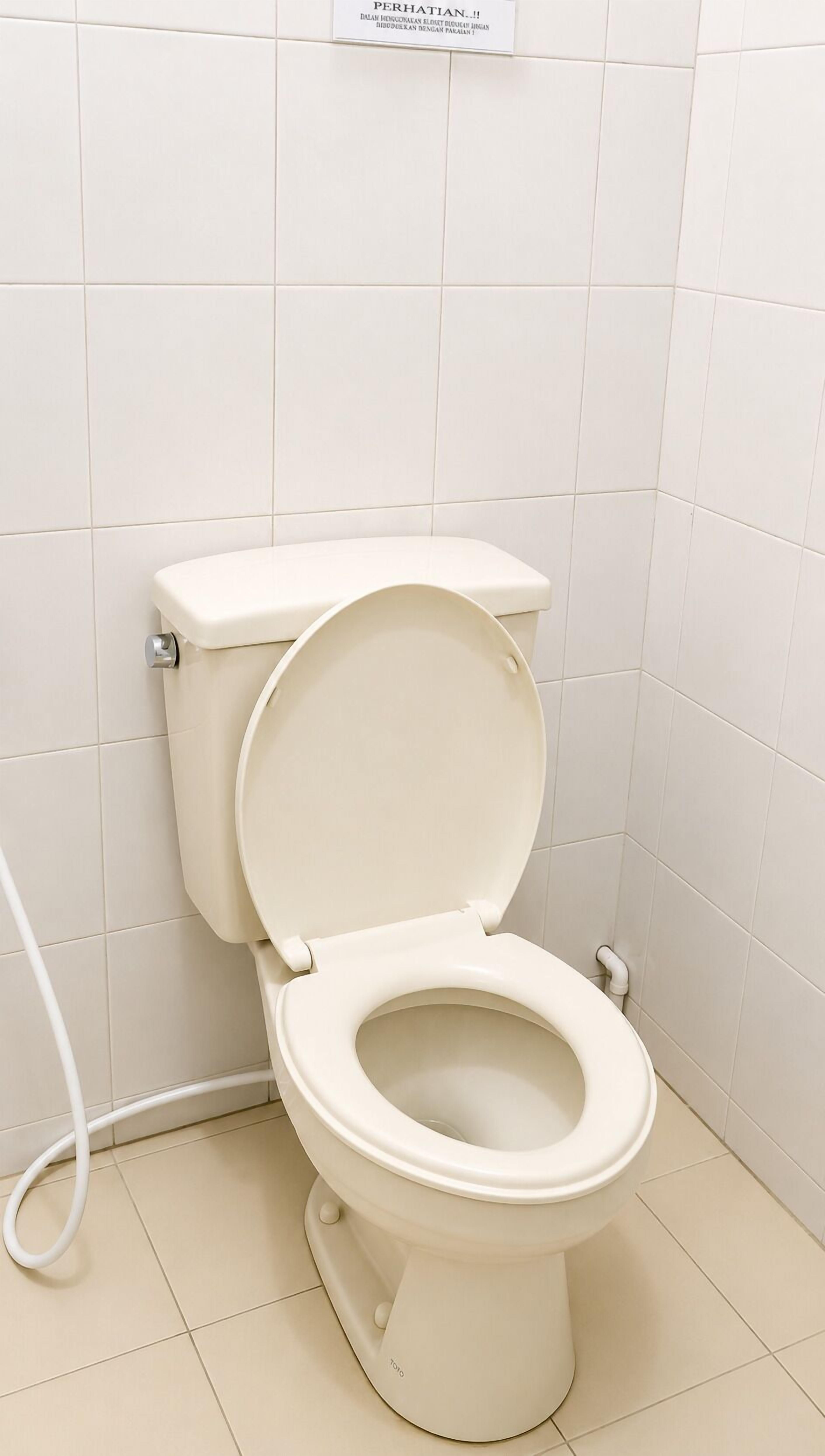 A toilet in a bathroom with white tiles on the walls and floor.