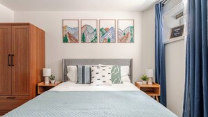 A bedroom with a large bed, a wooden wardrobe, and a wall with four framed artworks. - West Seattle Junction • Private Parking • Walkable • 15 mins from Downtown (Seattle)