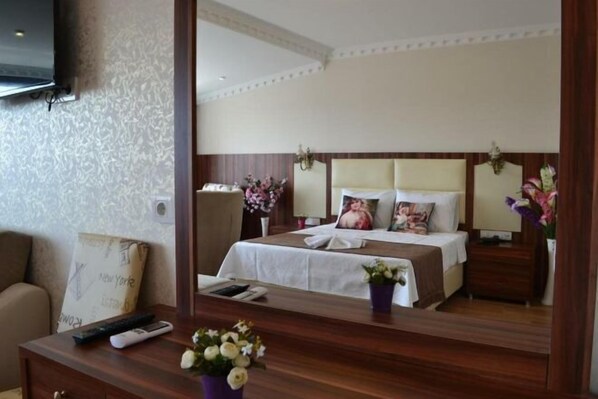 A hotel room with a bed, bedside tables, a mirror, a TV, and a desk with a vase of flowers.