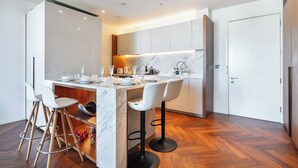 A modern kitchen with a marble island, white bar stools, and wooden flooring. - American Embassy Luxury 2 Bed 2 Bath Top Location! (London)