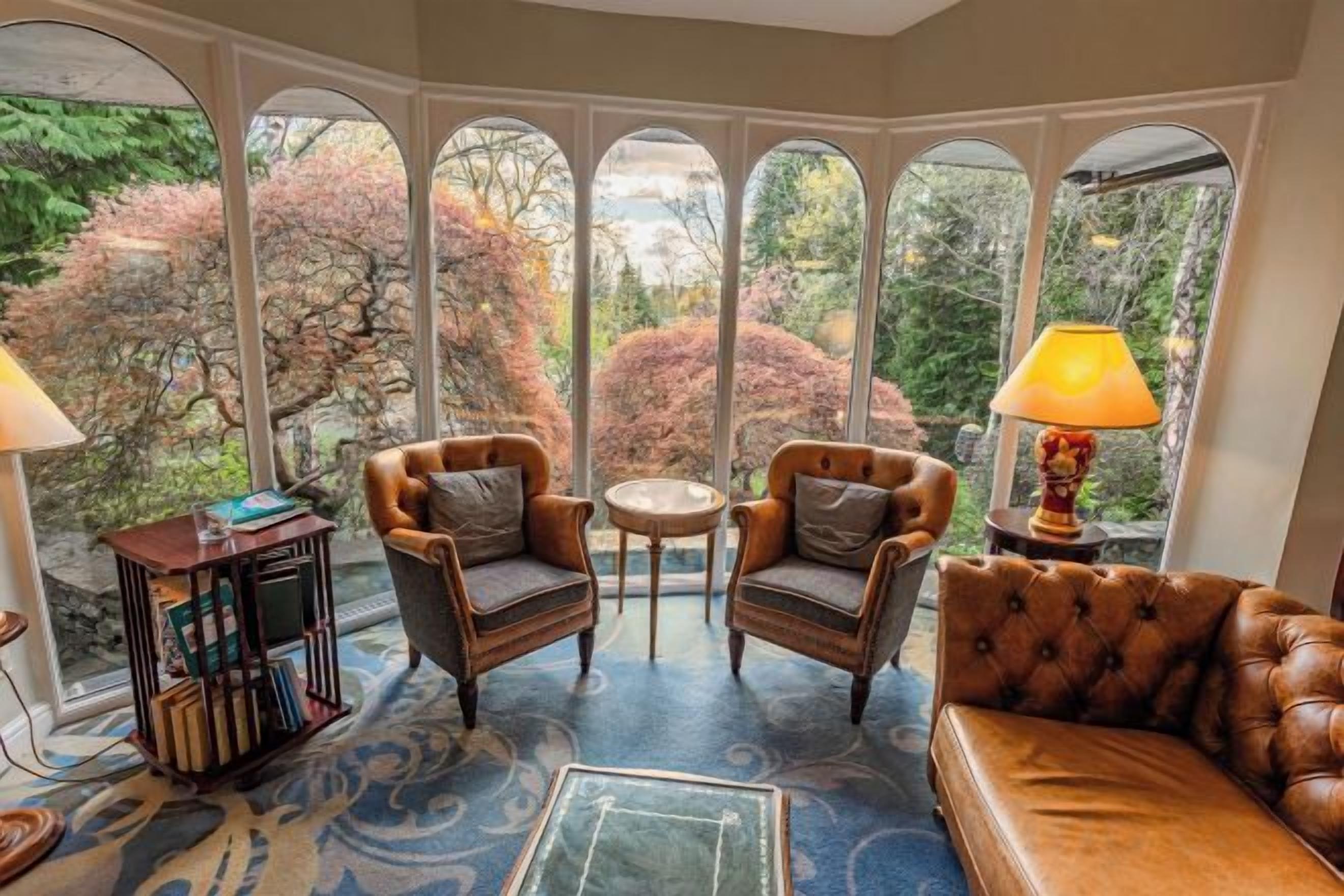 A room with a view through arched windows, two armchairs, a sofa, a small table, and a lamp.