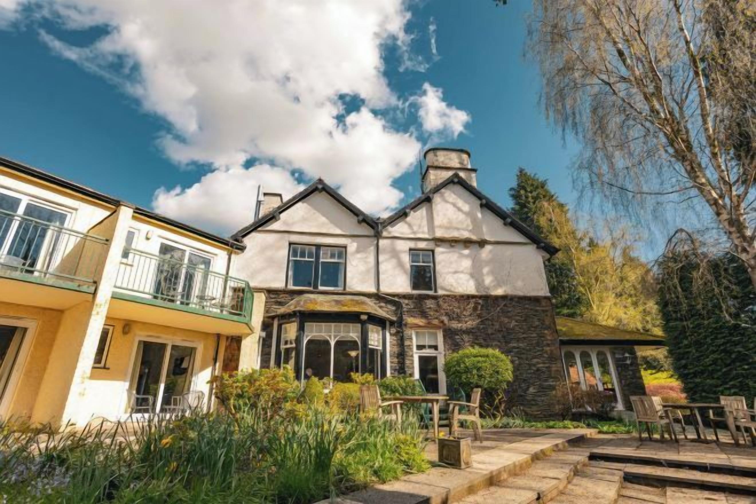 A two-story stone house with a balcony, a stone chimney, and a well-maintained garden.