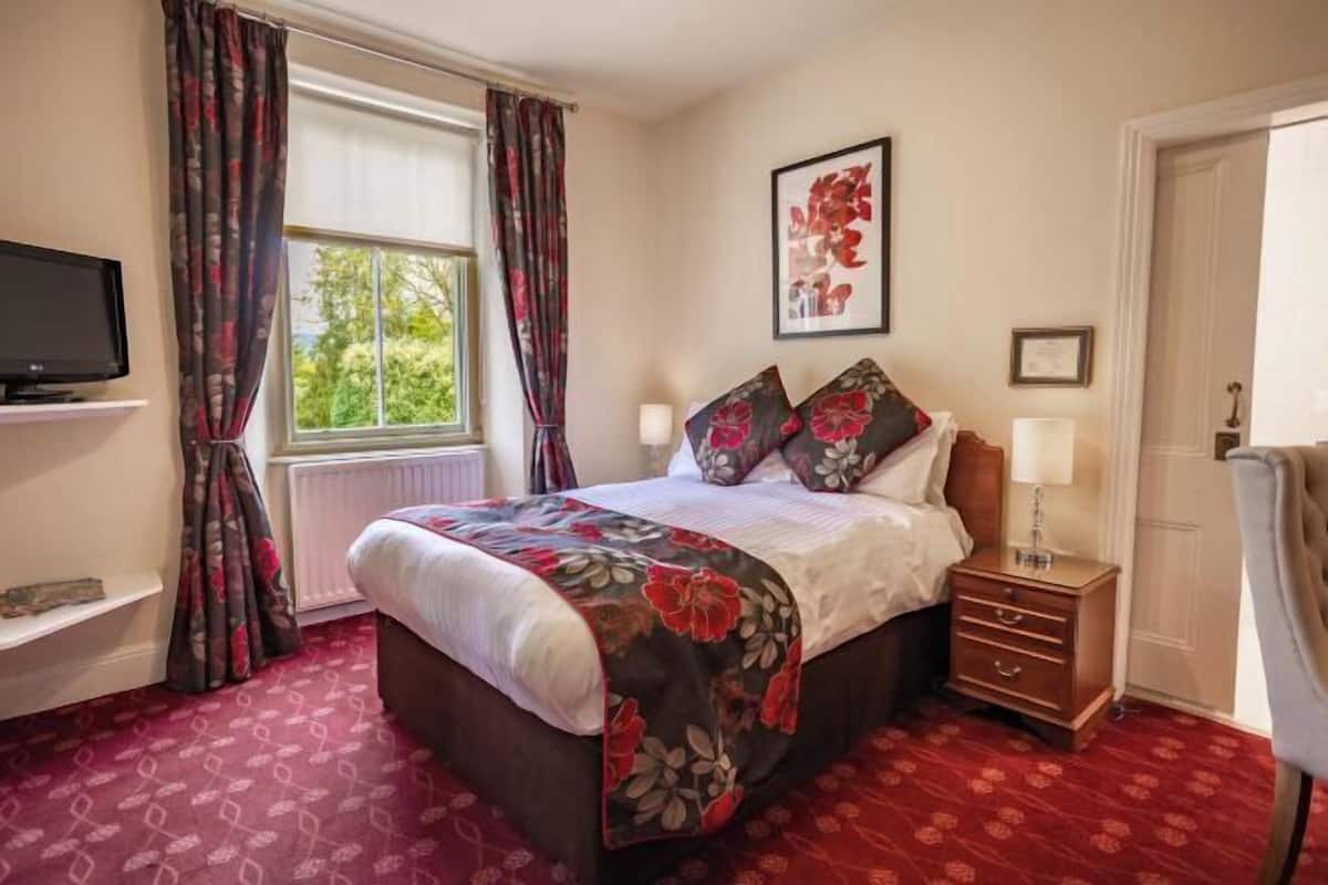 Un dormitorio con cama, mesita de noche, televisión y ventana con cortinas.