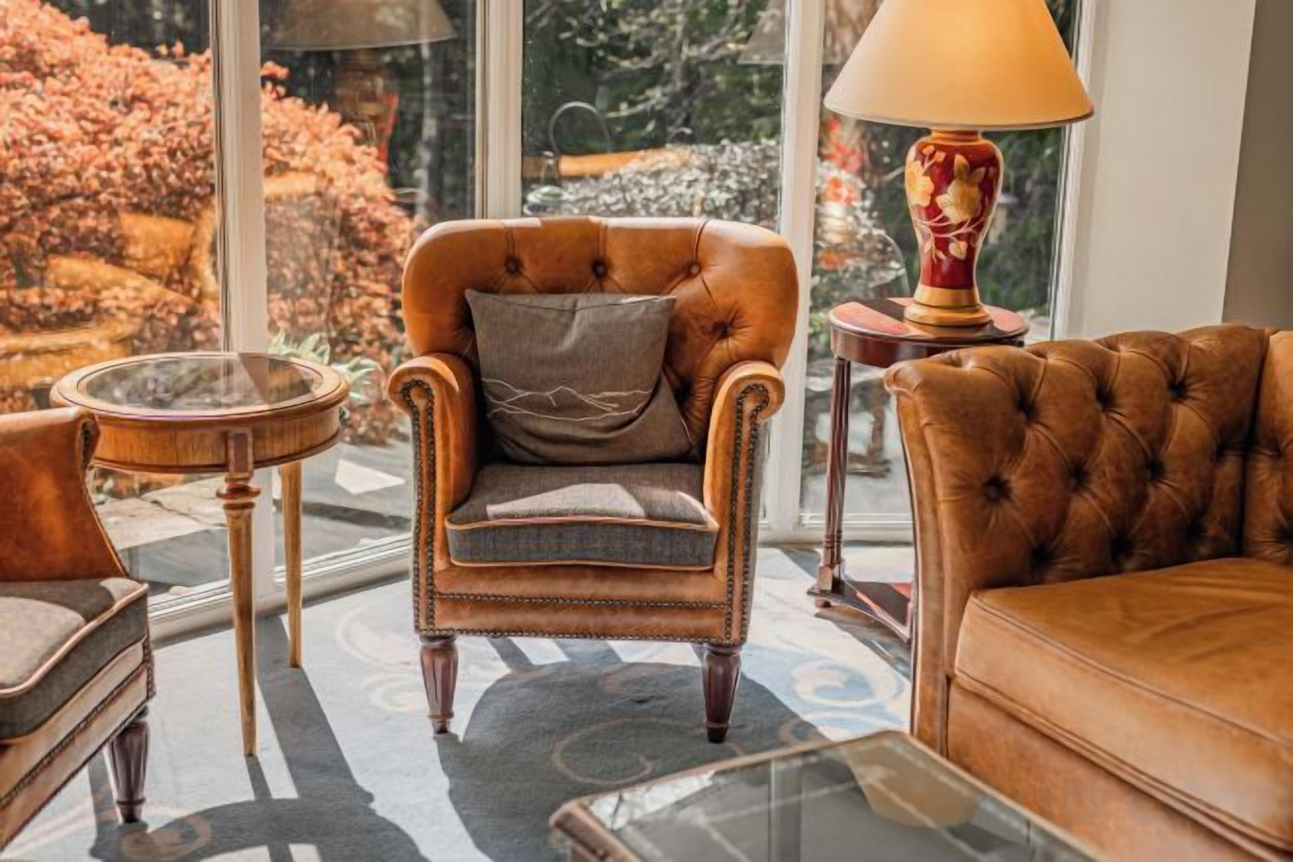 A room with a brown leather sofa, a tufted armchair, a round table, and a lamp.
