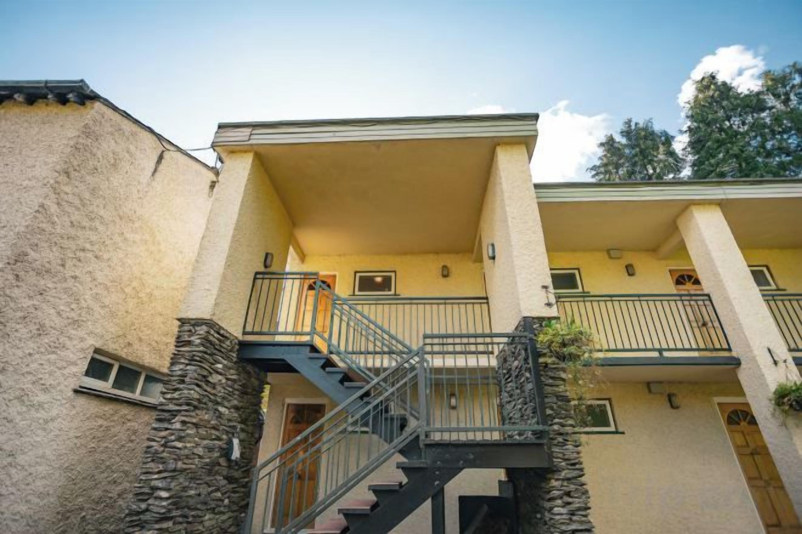 A two-story building with a balcony, a staircase, and stone pillars.