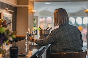 Iemand achter de bar met een drankje, een spoelbak en een raam met uitzicht.