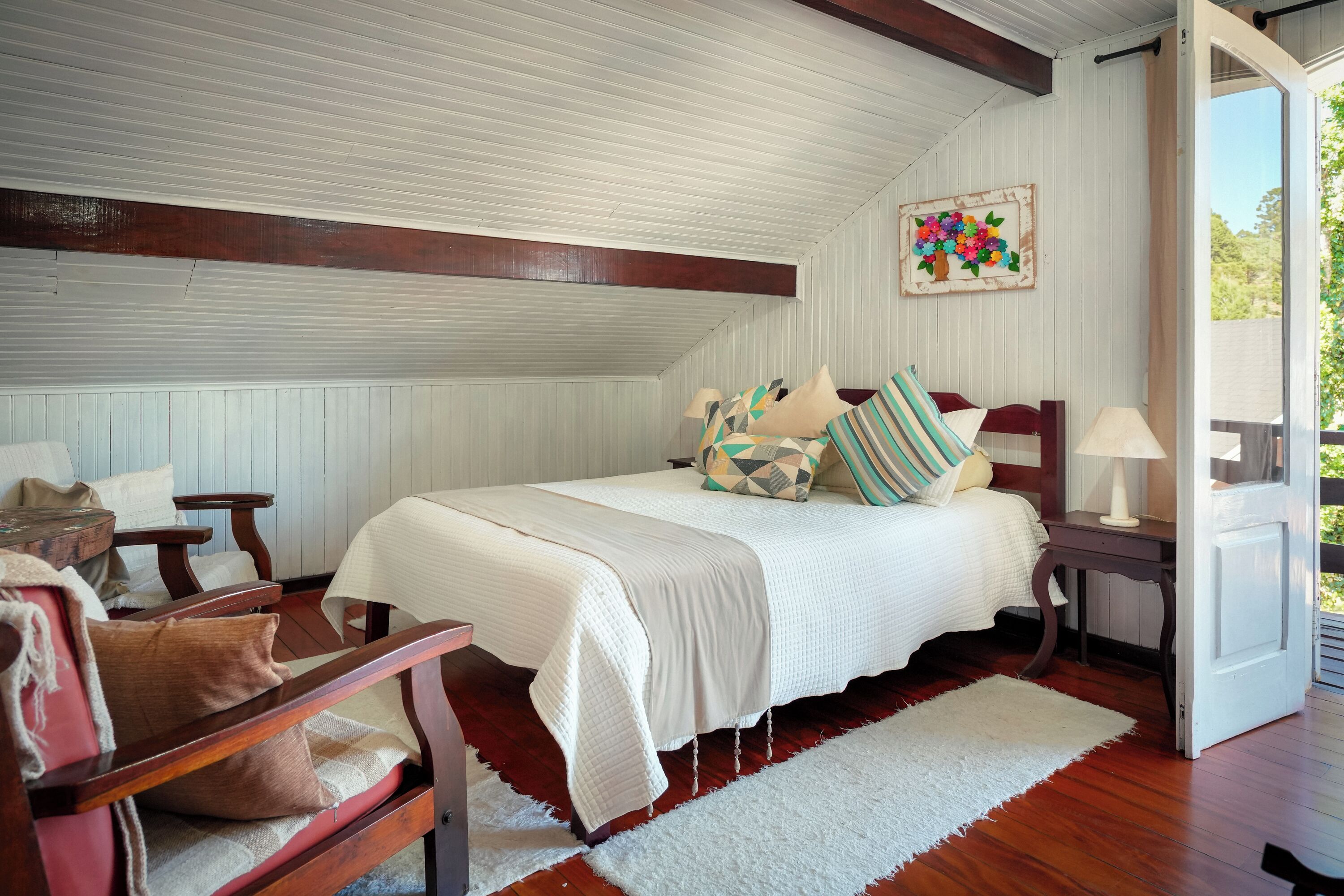 A bedroom with a bed, a chair, a nightstand, a lamp, and a door leading to an outdoor area.