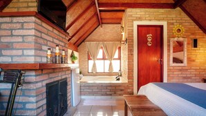 Una habitación acogedora con chimenea de ladrillo, un banco de madera, una cama y una puerta con espejo y elementos decorativos.