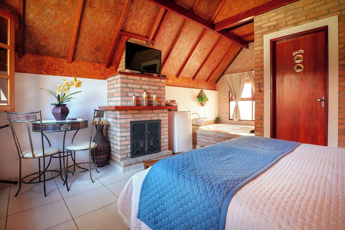 Una habitación acogedora con chimenea de ladrillo, un televisor montado en el techo, una cama con colcha azul y blanca, y una puerta de madera.