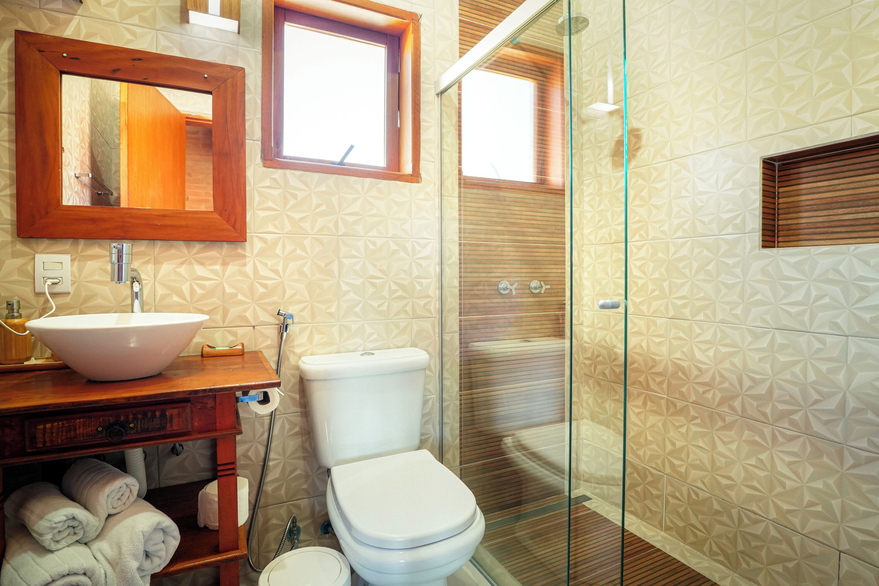 Un baño con tocador de madera, un espejo grande, un lavabo blanco y una ducha con cerramiento de vidrio.
