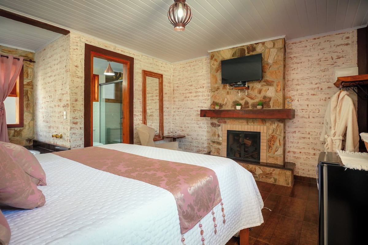 Un dormitorio con una cama grande, un televisor montado en una pared de piedra, una chimenea y un espejo.