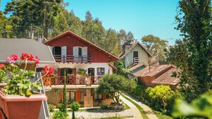 Una casa de estilo chalete tradicional con balcón, rodeada de abundante vegetación y un cielo despejado.