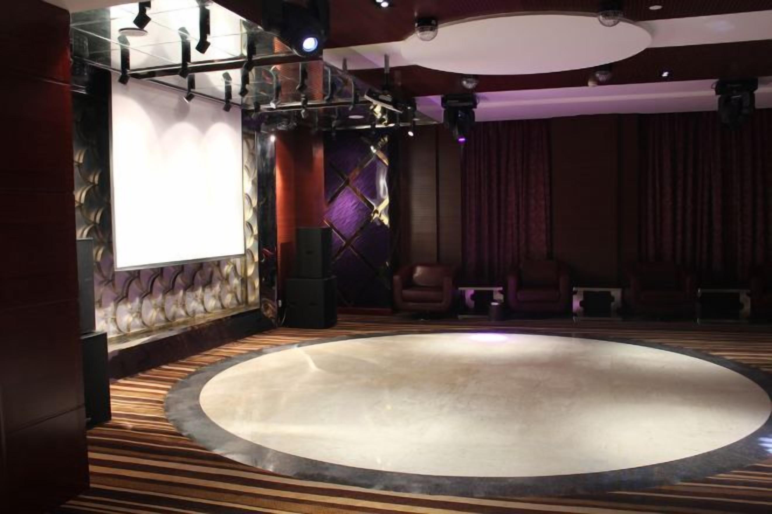 A theater with a circular stage, rows of seating, and a large screen.