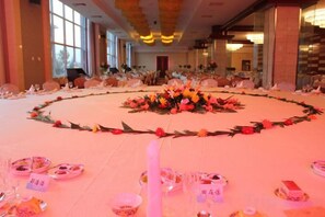 Une salle de banquet avec des tables rondes dressées pour un événement formel, agrémentées de compositions florales et d’une décoration de table soignée.
