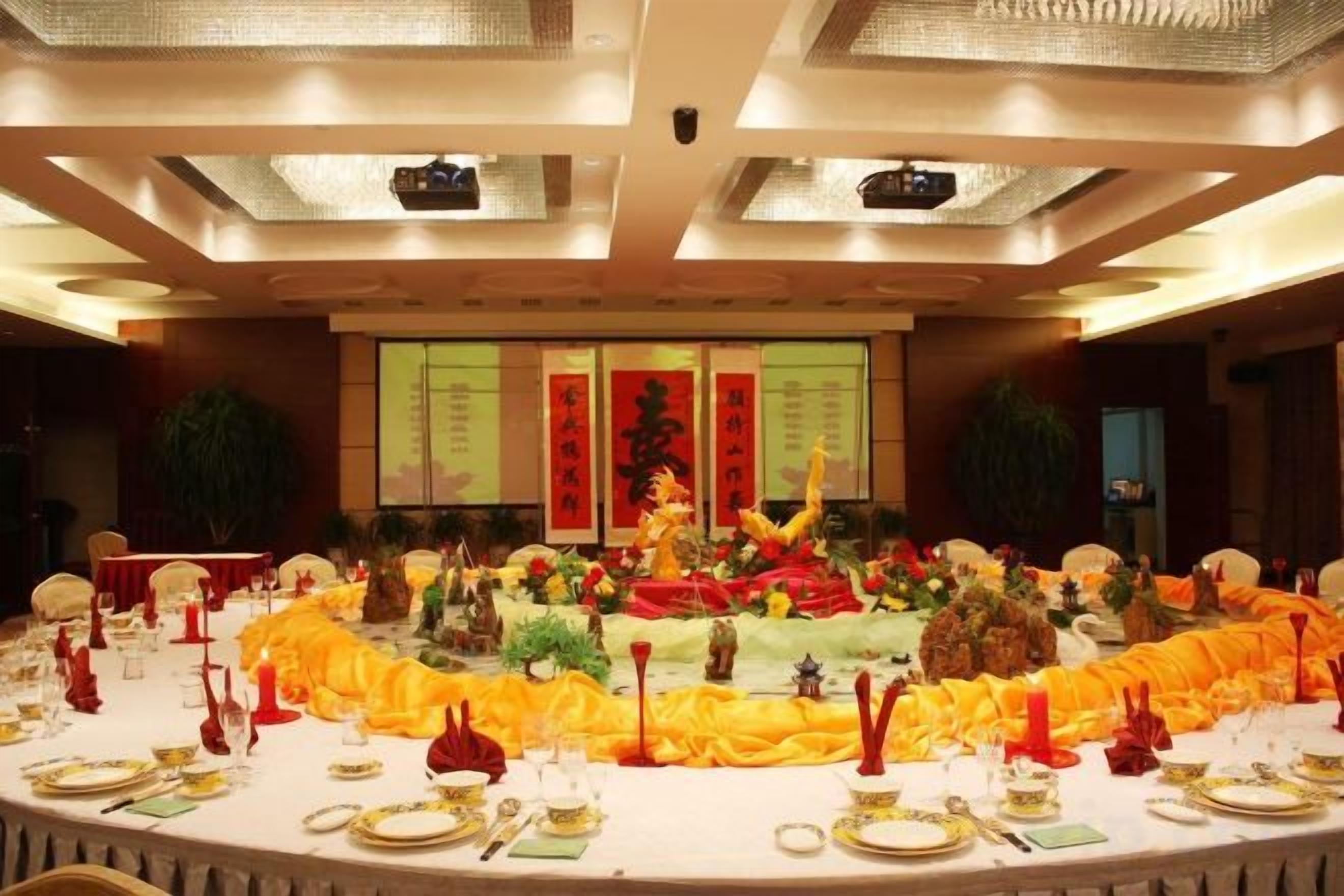 A banquet hall with a round table set for a formal event, featuring a central decorative arrangement and a backdrop with Chinese characters.