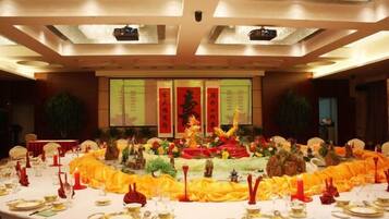 A banquet hall with a round table set for a formal event, featuring a central decorative arrangement and a backdrop with Chinese characters.