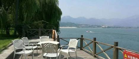 A wooden deck with outdoor seating, overlooking a body of water and distant mountains.
