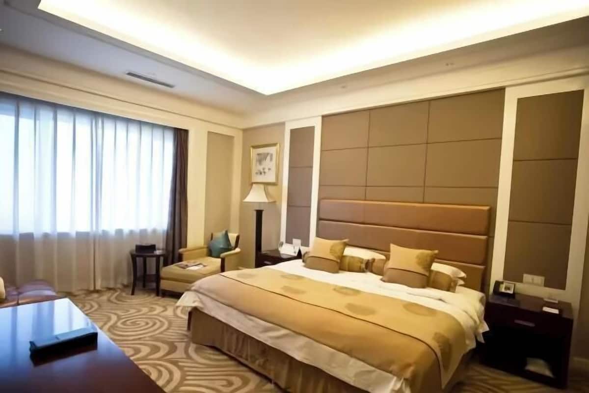 A hotel room with a large bed, a desk, a chair, a lamp, and a window with curtains.