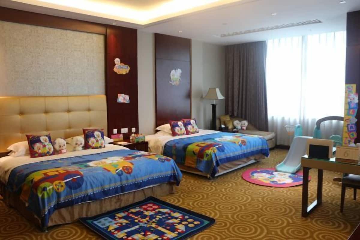 A hotel room with two beds, a desk, a chair, a lamp, and a window with curtains.