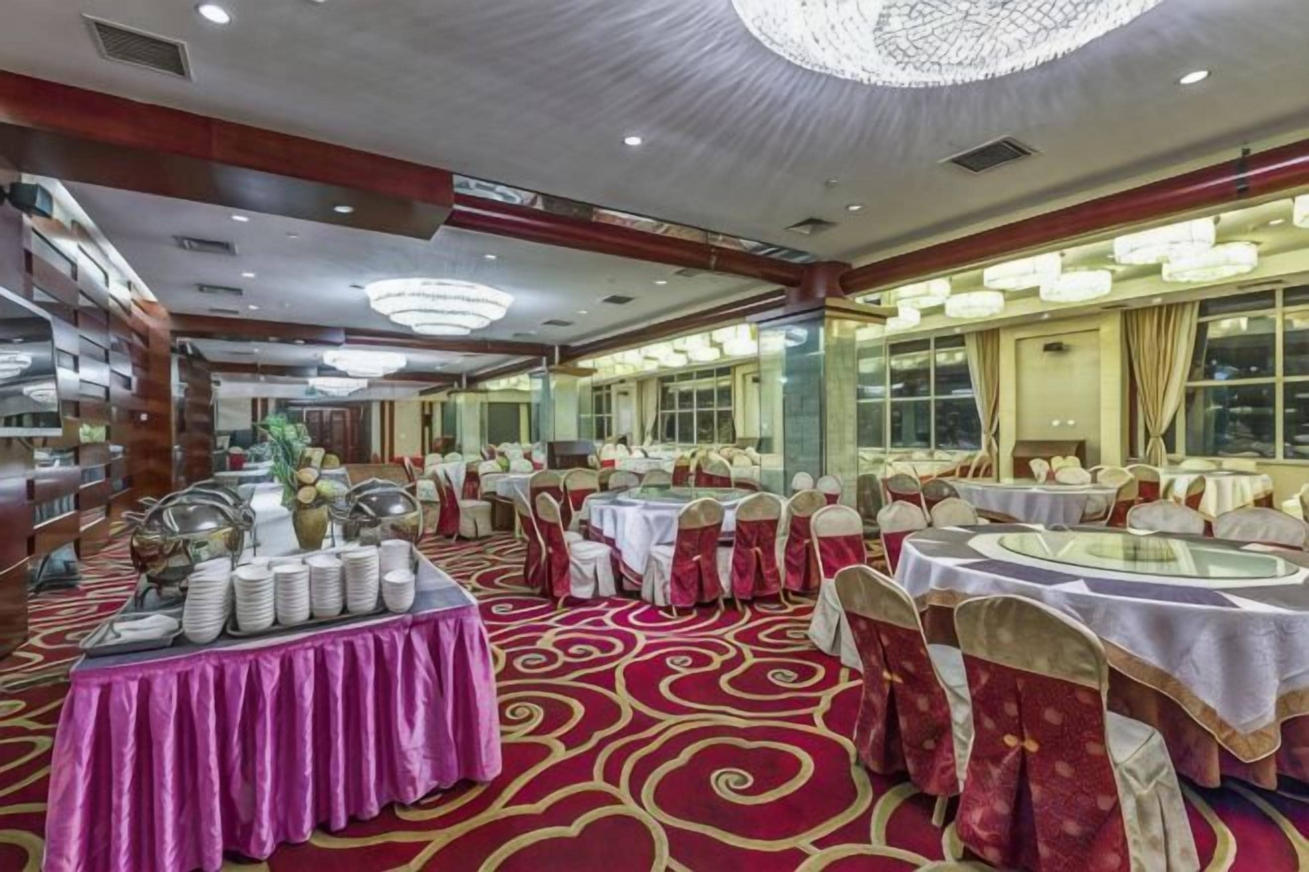 Un salón de banquetes con mesas redondas, sillas y una barra de buffet.