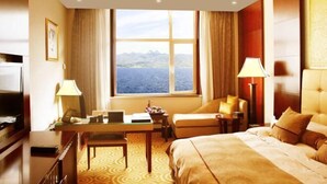 Een hotelkamer met een bed, een bureau met een laptop, een stoel, een televisie en uitzicht op zee.
