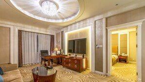 Een hotelkamer met een ronde salontafel, een bank, een televisie, een dressoir en een kamerbreed tapijt met dessin.