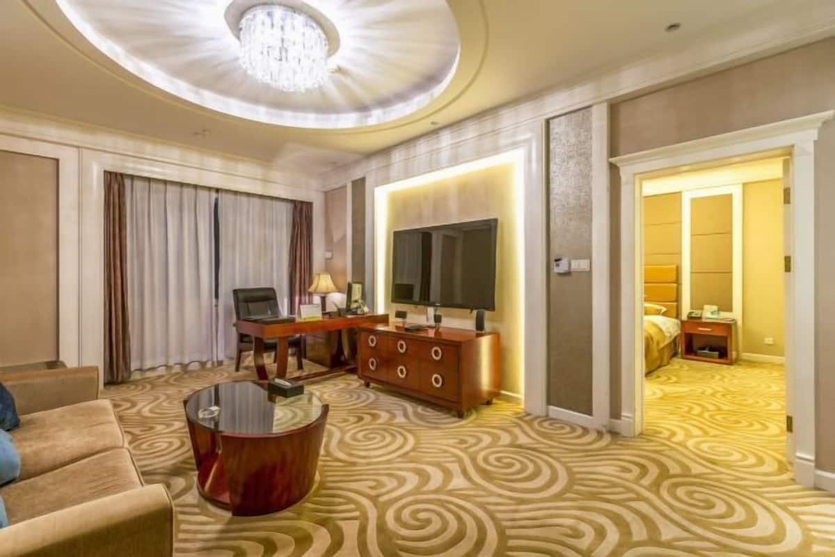 A hotel room with a round coffee table, a sofa, a TV, a dresser, and a patterned carpet.