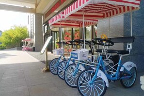 A row of blue bicycles parked under a red and white striped awning, with a signboard and a pink bicycle in the background. - Xuehu Garden Hotel (Jinan)