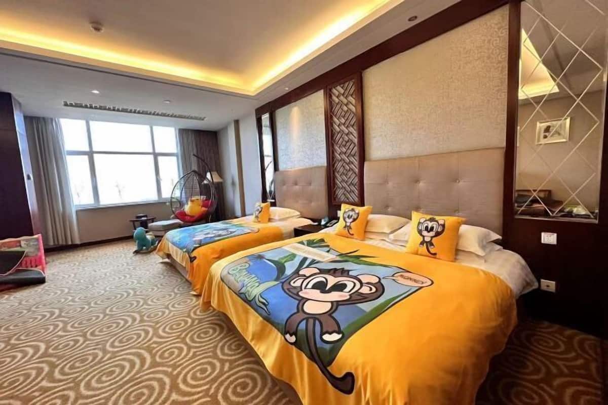 A hotel room with two beds, each with a cartoon monkey bedspread, a large window, and a view of the outdoors.