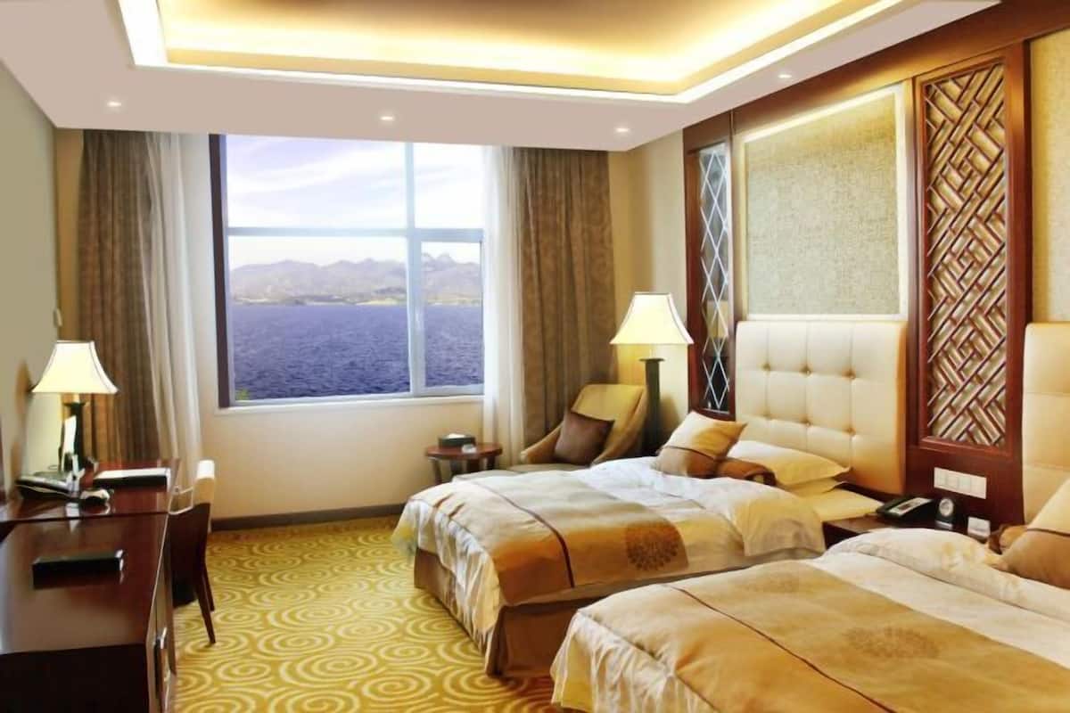 A hotel room with two beds, a desk, and a view of the sea.