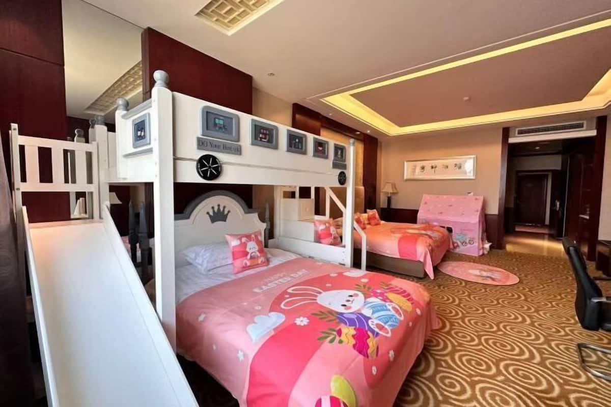 A hotel room with bunk beds, a small desk, and a bed with a colorful bedspread.