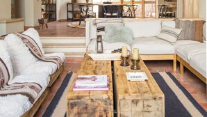 Ein geräumiger Wohnbereich mit hoher Decke, Holzbalken und einem Balkon. Zwei Sofas, ein Couchtisch und ein Esstisch mit Stühlen sind vorhanden.