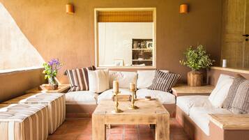 A cozy living area with a sofa, ottomans, a wooden coffee table, and a large window.