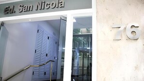 Entrada de um edifício com uma placa indicando "Ed. San Nicolas" e o número grande "76" na parede.