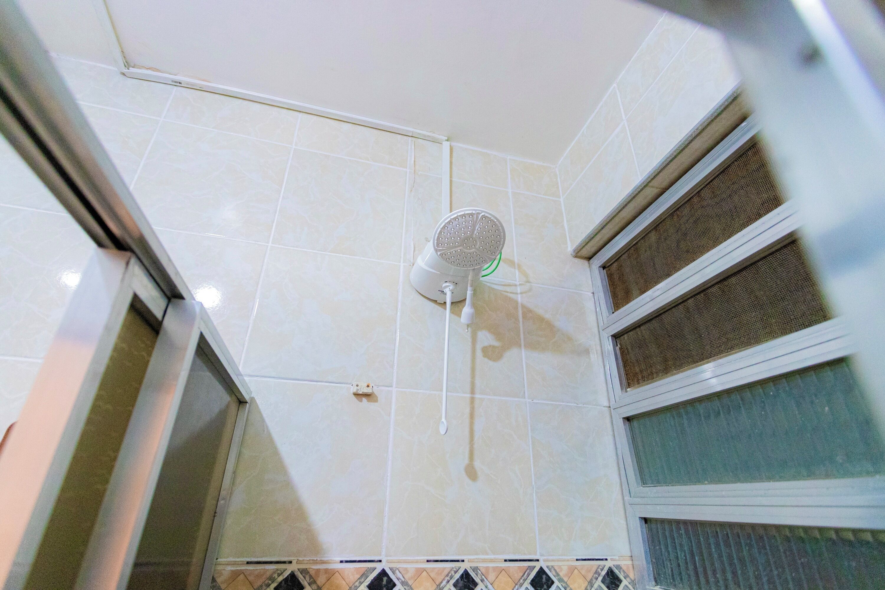 Una ducha con cabezal de ducha de mano, paredes con azulejos y una ventana con persianas.
