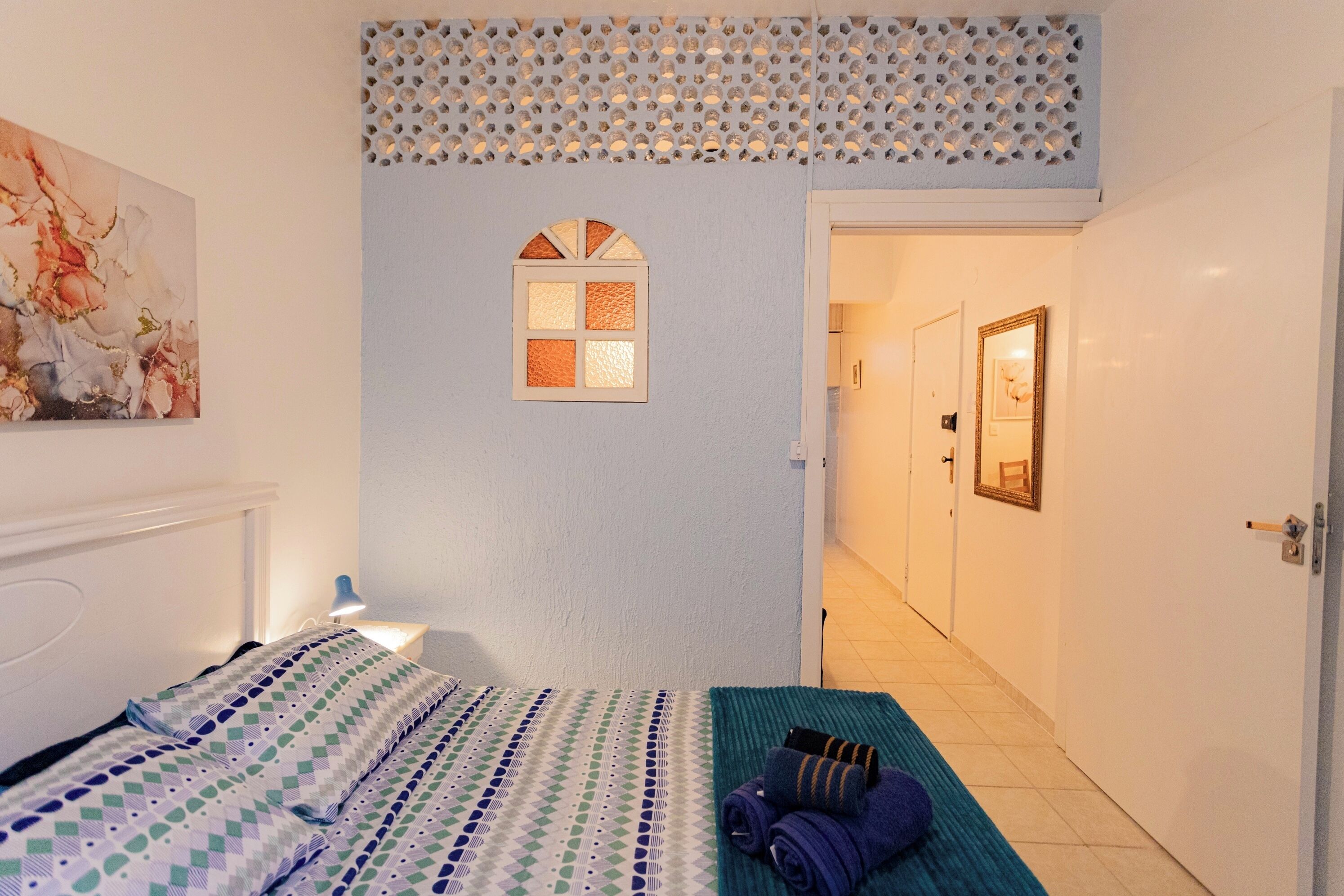Ein Hotelzimmer mit Bett, einem Fenster mit Zierrahmen, einem Handtuchhalter und einem Flur, der zu einem anderen Zimmer führt.