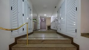 Corredor de hotel com escadaria de mármore, armários brancos e corrimão dourado.