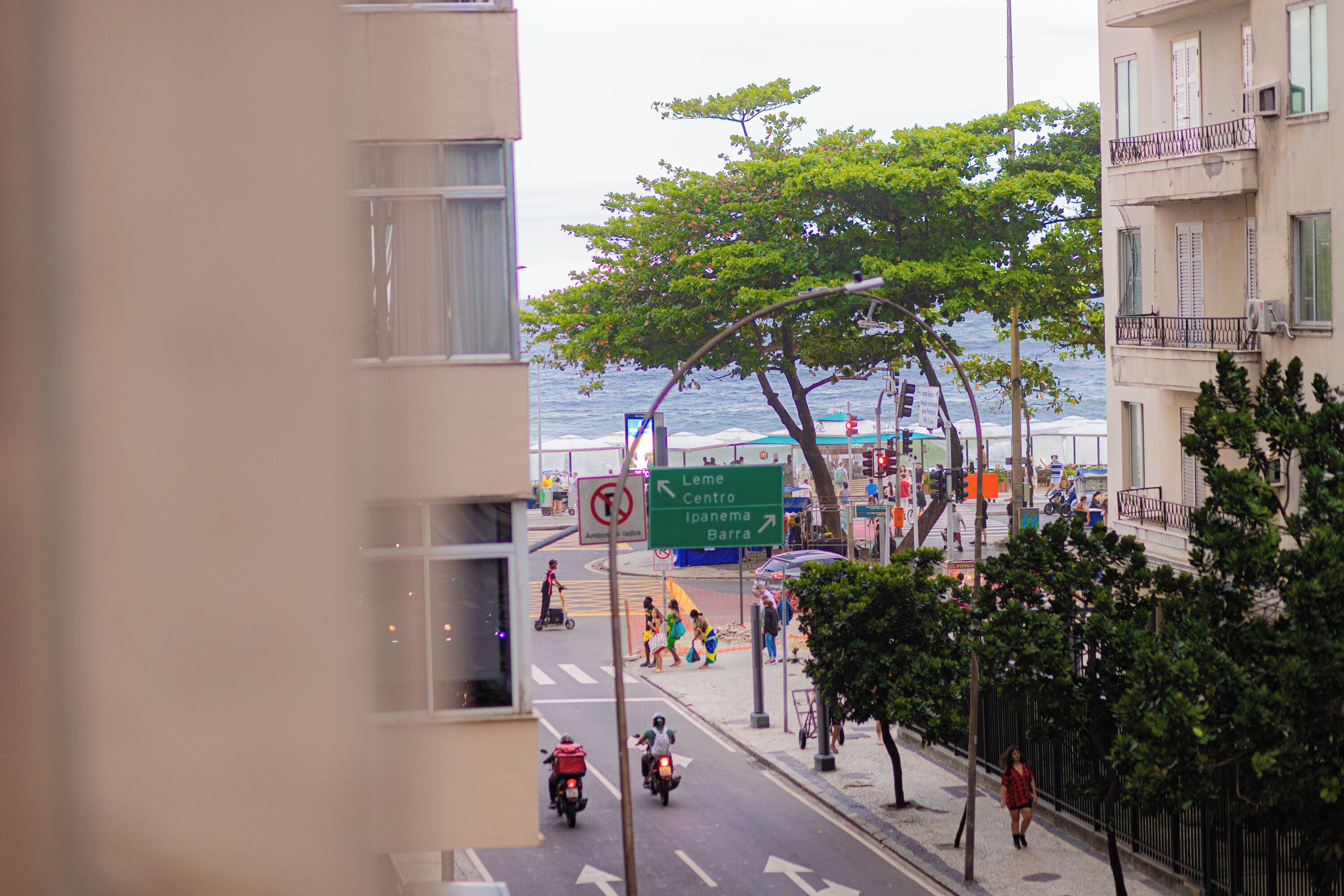 Calle con vista al océano, un cartel que indica direcciones a Leme Centro, Ipanema y Barra, y un paso de peatones.