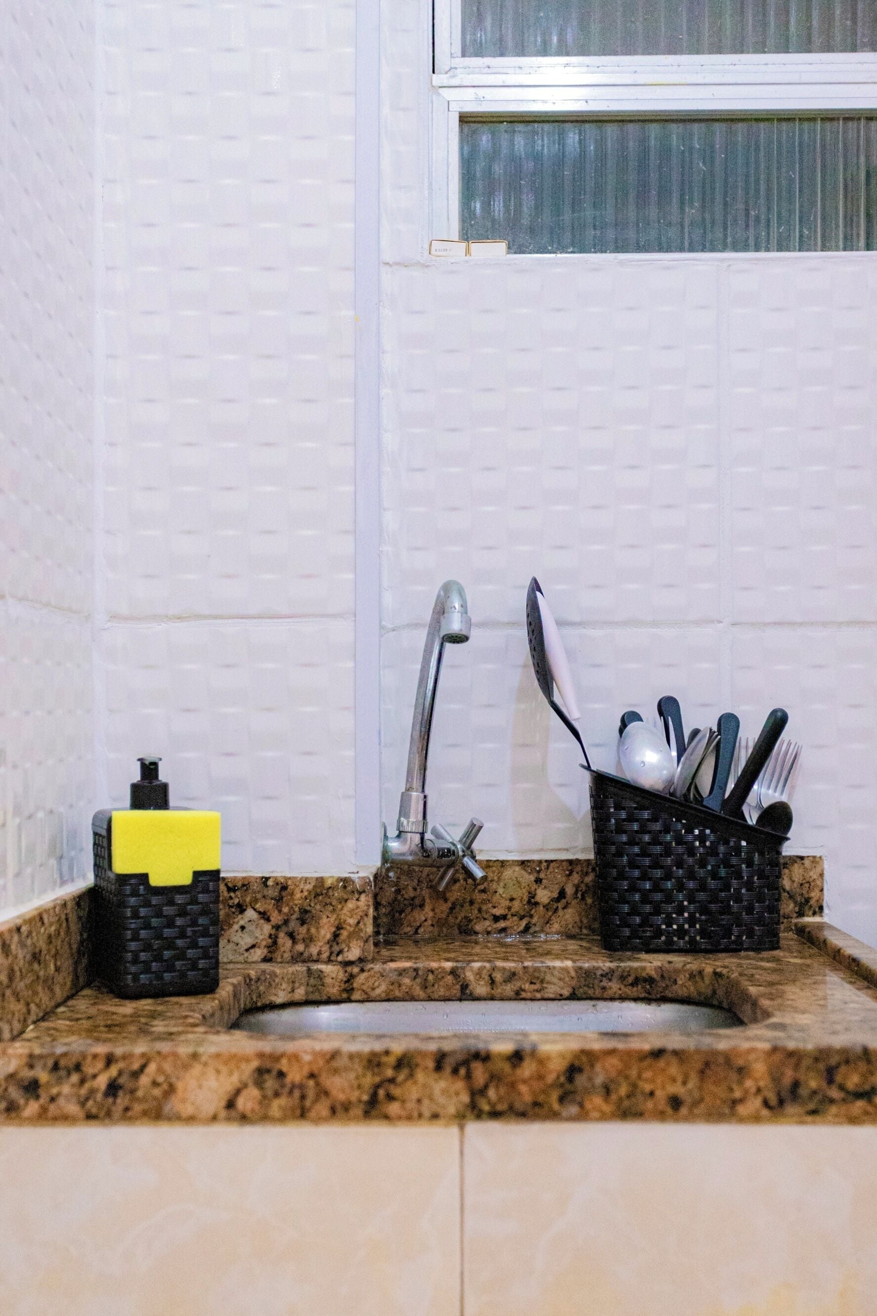 A kitchen with a granite countertop, a stainless steel faucet, a yellow sponge, and a utensil holder.